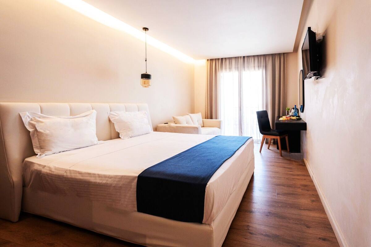 A hotel room with a large bed, a desk, and a TV on the wall.