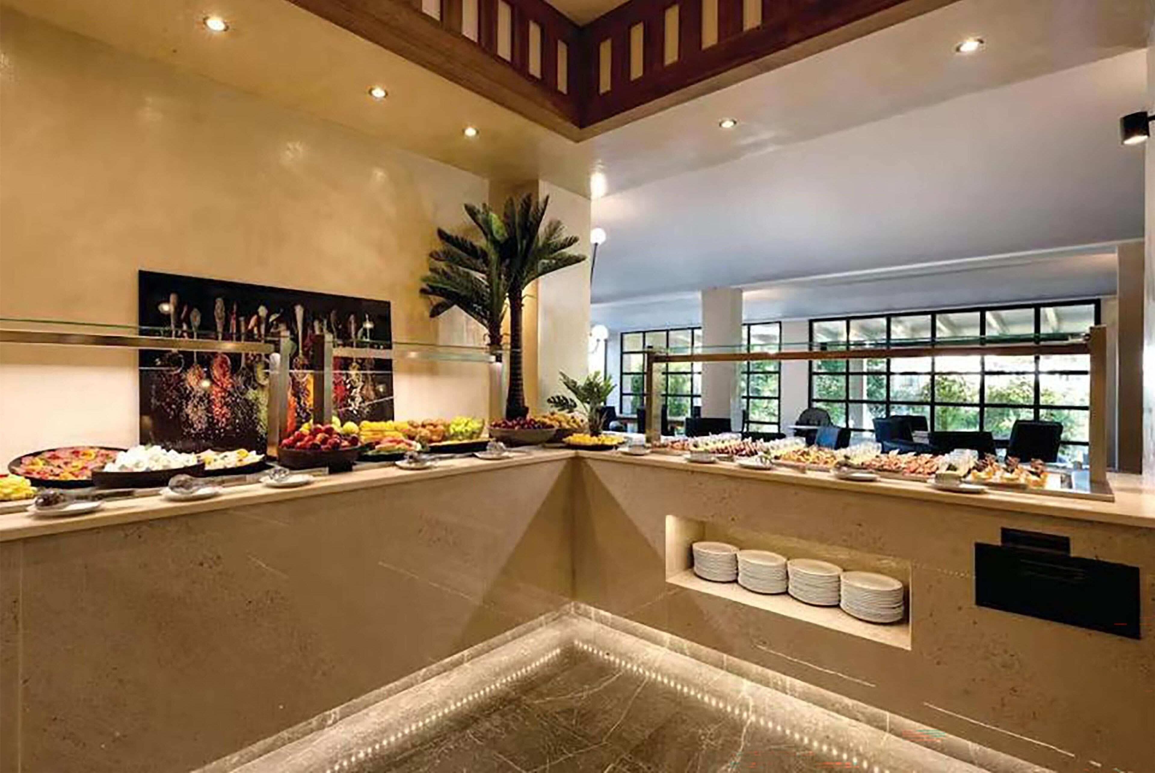 A buffet area with various food items, a large painting, and a palm tree.