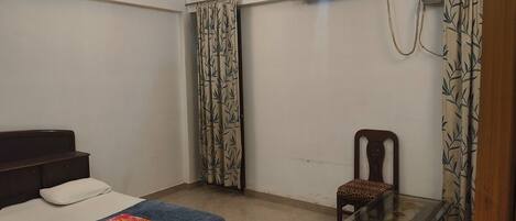 A bedroom with a bed, a chair, a small table, and an air conditioning unit.