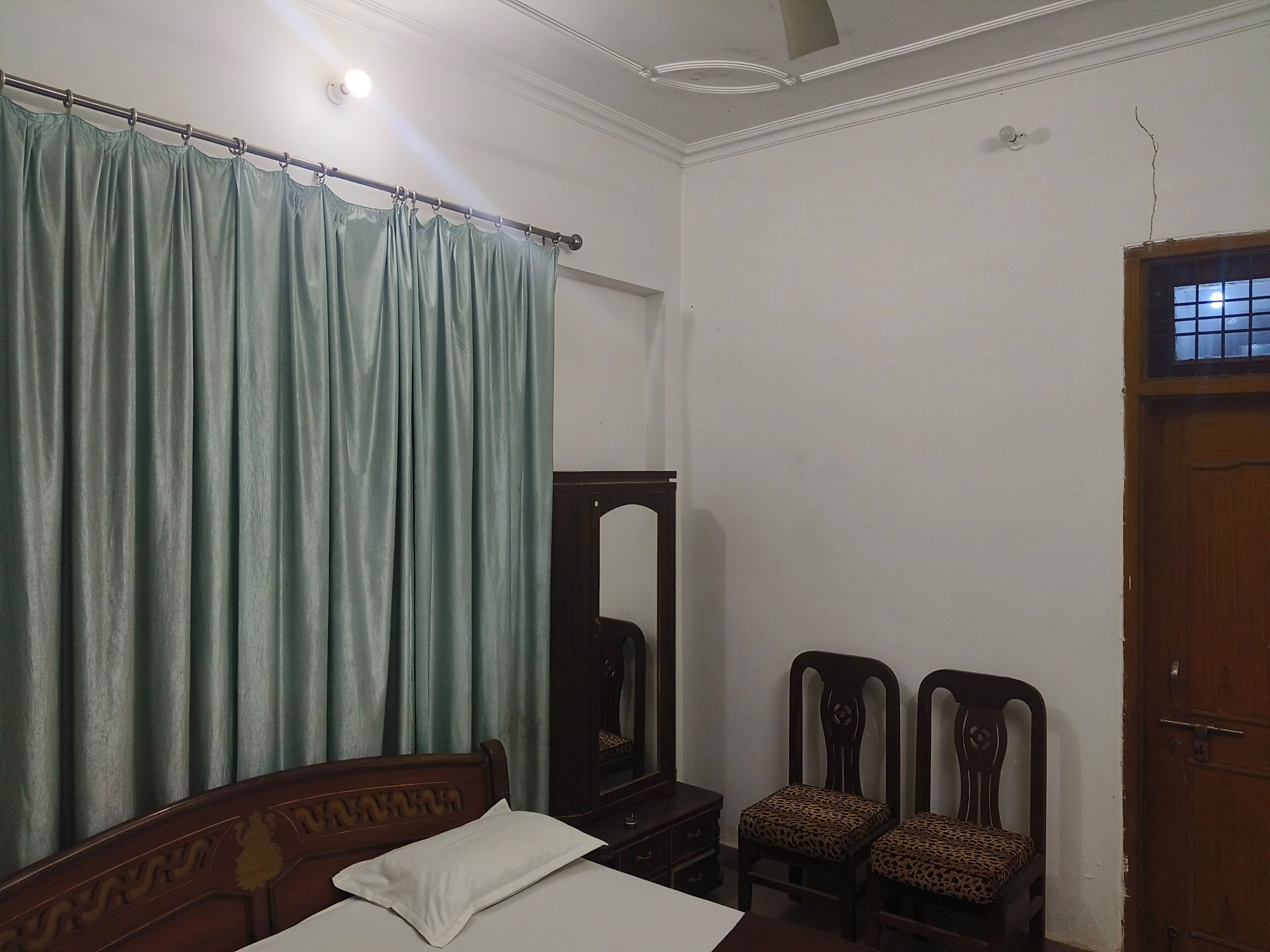 Een slaapkamer met een bed, een houten garderobe, twee stoelen met gestreepte kussens, een spiegel en een deur.