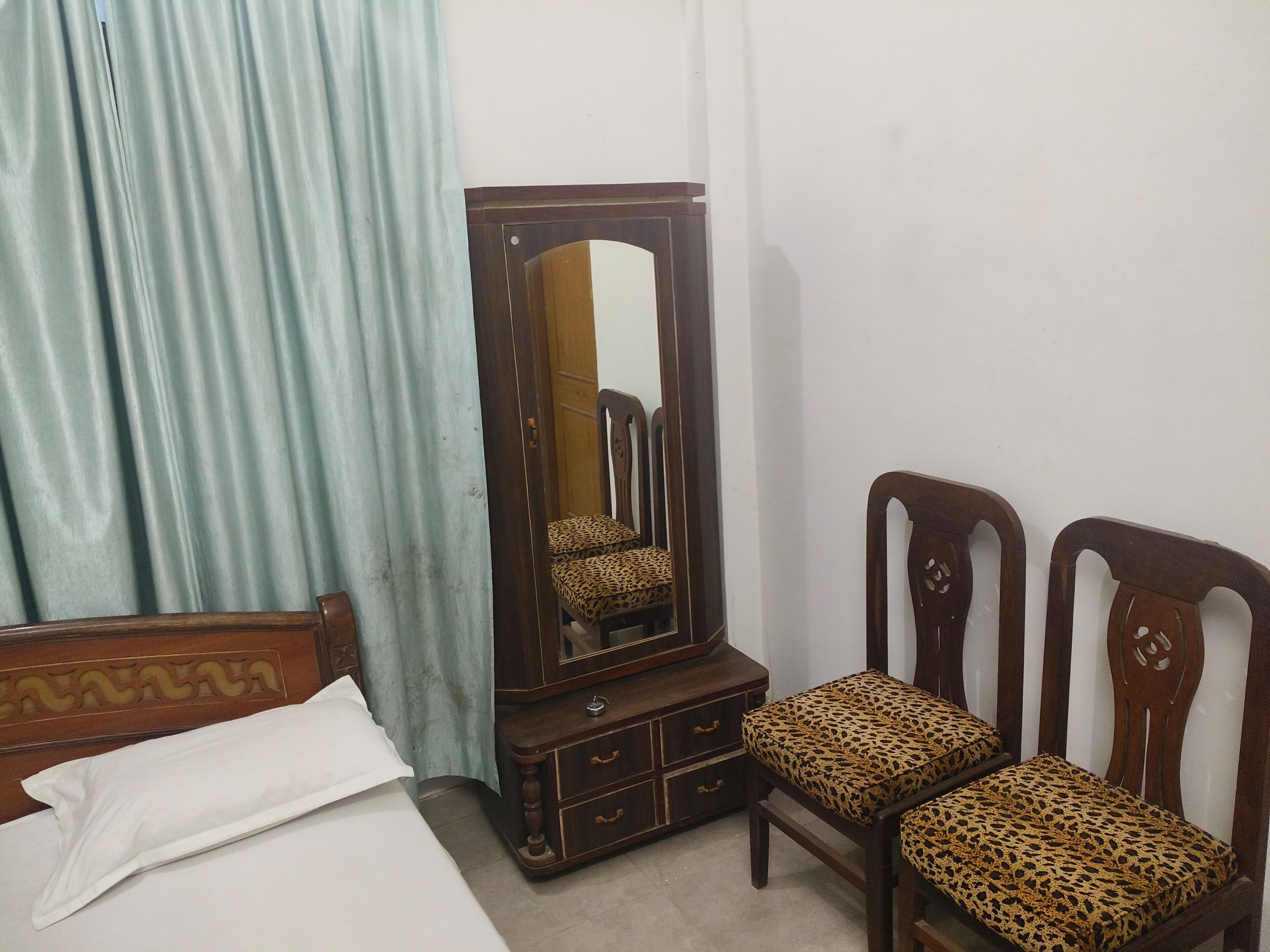 A bedroom with a bed, a wooden dresser with a mirror, two leopard print chairs, and a blue curtain.