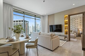Een moderne woonkamer met een bank, een eettafel, een aan de muur bevestigde televisie en een stadszicht door grote ramen.
