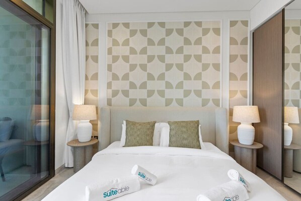 A hotel room with a large bed, two bedside tables with lamps, a patterned wall, and a view through a glass door.