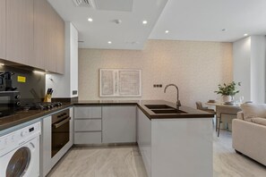 Een moderne keuken met een inbouwfornuis, spoelbak en vaatwasser, een eetgedeelte met een tafel en stoelen, en een woonkamer met een bank.