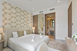 A modern hotel room with a large bed, a bedside table, a mirror, and a view into the bathroom.