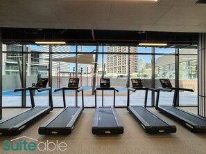 A gym with five treadmills aligned in a row, large windows, and a visible outdoor view.