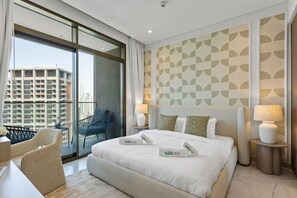 A modern hotel room with a large bed, two bedside lamps, a chair, and a view of the city through floor-to-ceiling windows.