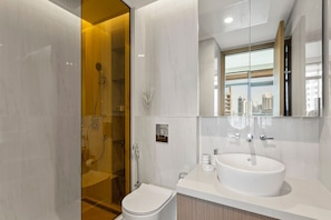 A modern bathroom with a glass-enclosed shower, a white sink, and a large mirror reflecting the cityscape.
