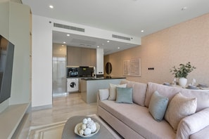 En moderne stue med en beige sofa, et sofabord og et køkken i baggrunden.