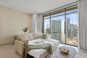 Un salon moderne avec un canapé, une petite table agrémentée d’objets décoratifs et une vue sur le paysage urbain, visible à travers de grandes fenêtres.