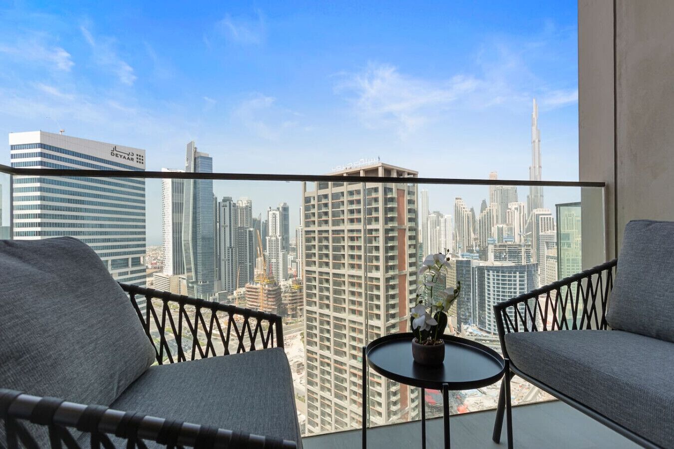 Een balkon met twee grijze banken, een klein rond tafeltje met een plant in pot en uitzicht op een stadsgezicht, waaronder de Burj Khalifa.