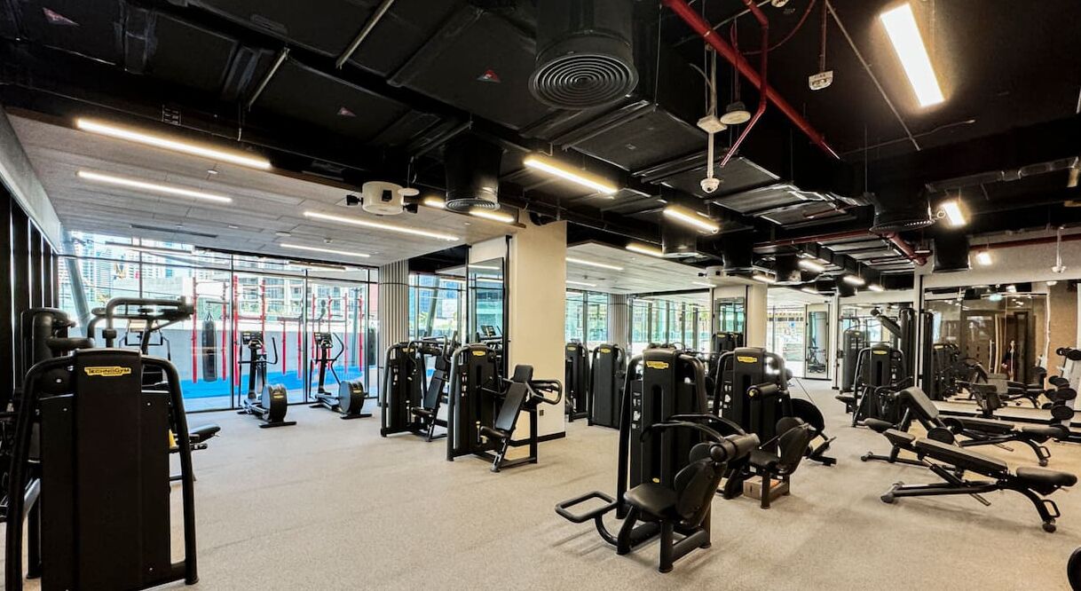 A gym with various exercise equipment, large windows, and a mirror wall.