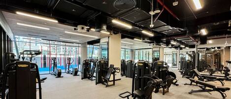 A gym with various exercise equipment, large windows, and a mirror wall.