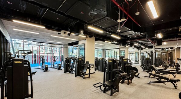 Een fitnessruimte met diverse trainingsapparaten, grote ramen en een spiegelwand.