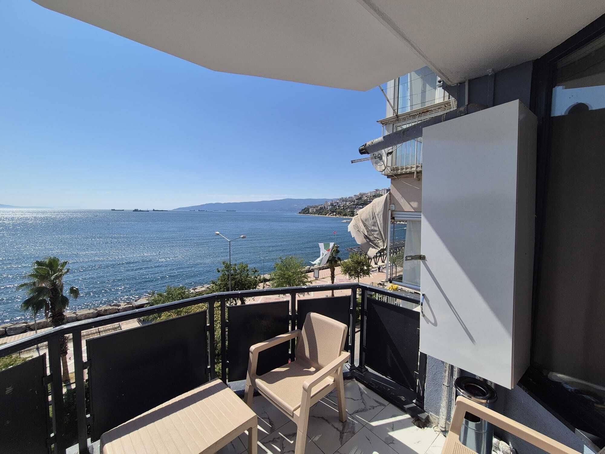 Un balcón con vista al mar, una silla y una mesa.