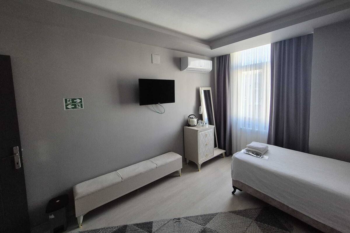 Habitació d'hotel amb llit, una panxa, televisió, mirall i finestra amb cortines.