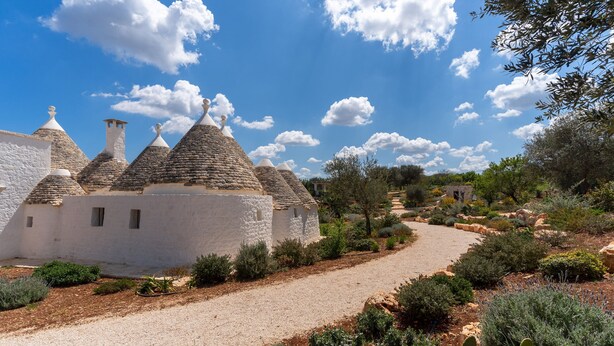 A traditional white building with conical roofs, surrounded by a gravel path and various shrubs. - Trulli Pietra Rossa With Pool by Wonderful Italy (Ostuni)