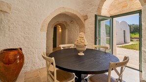 A round table with chairs in a room with white walls and arches. A large vase is on the table. - Trulli Pietra Rossa With Pool by Wonderful Italy (Ostuni)