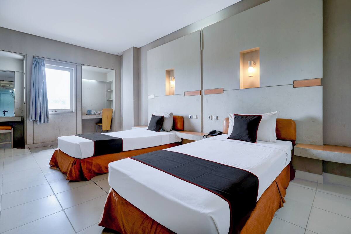 Habitación de hotel con dos camas, un espejo grande, una ventana con cortinas y un escritorio pequeño con una silla.