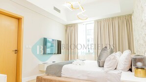 A modern bedroom with a bed, a TV, a bedside table, and a window with curtains. - Bloomfields Mayan 3BR Beach Access YAS (Abu Dhabi)