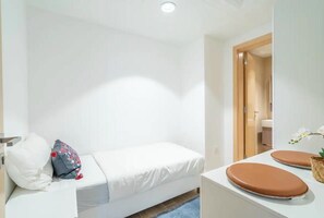 A small, clean room with a single bed, a white wall, and a wooden door leading to a bathroom. - Bloomfields 2BR+1 in Mayan (Abu Dhabi)