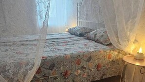 A bedroom with a bed, a bedside table with a candle, and sheer curtains.