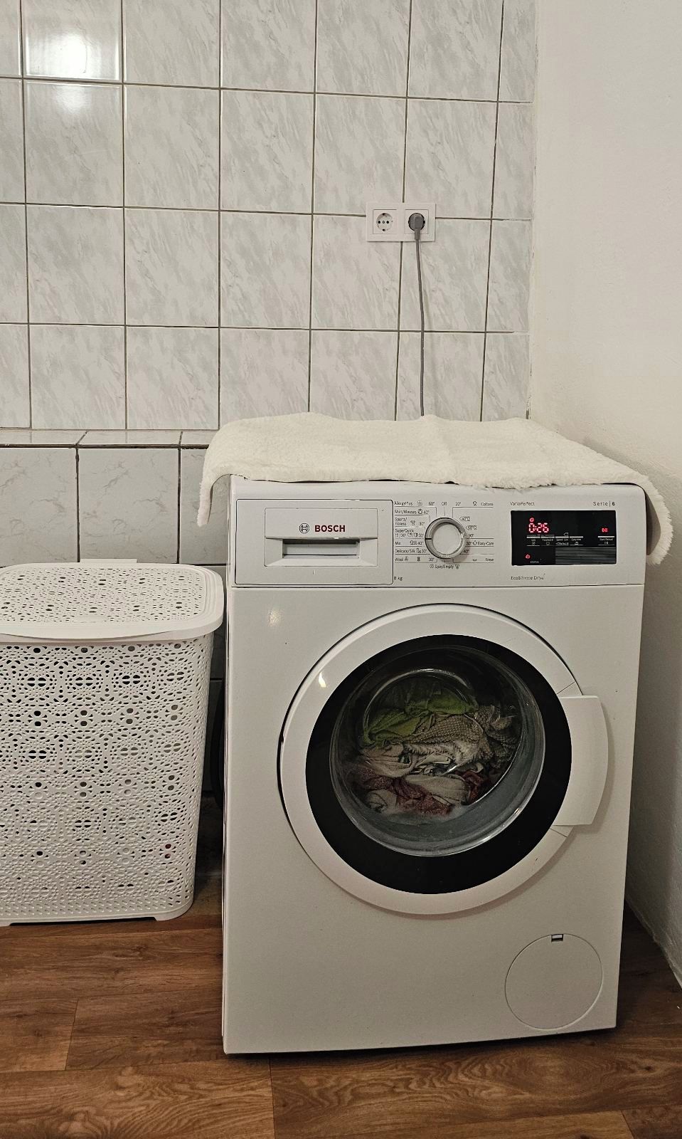 A Bosch washing machine in a bathroom with tiled walls and a wooden floor.