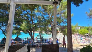 A beachside area with a pergola, seating, and a view of the beach and sea.