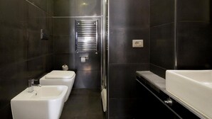Un baño moderno con azulejos oscuros, un lavabo blanco, un inodoro y una zona de ducha.