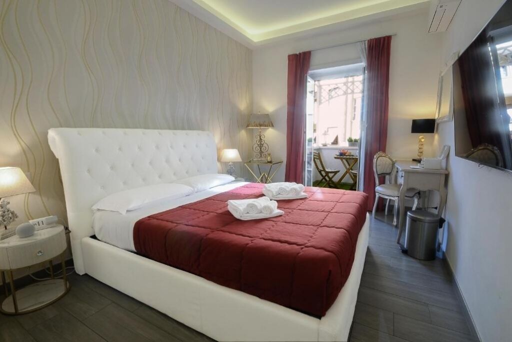 Ein Hotelzimmer mit einem großen Bett, einem Nachttisch, einer Lampe und Blick ins Freie.