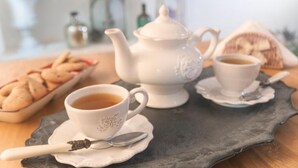Una mesa con un calentador de té, dos tazas de té y un plato de galletas.