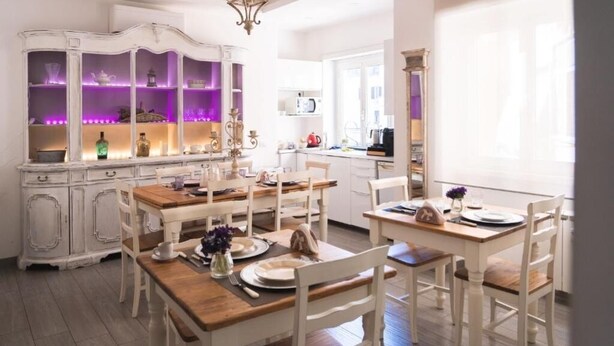 Un comedor con muebles de madera blanca, un armario blanco con iluminación morada y una araña.