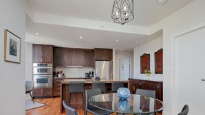 A modern kitchen with dark wooden cabinets, stainless steel appliances, and a glass dining table with black chairs.
