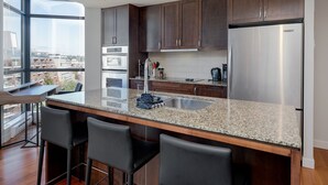 A modern kitchen with dark wood cabinets, stainless steel appliances, a granite countertop, and a large window offering a city view.