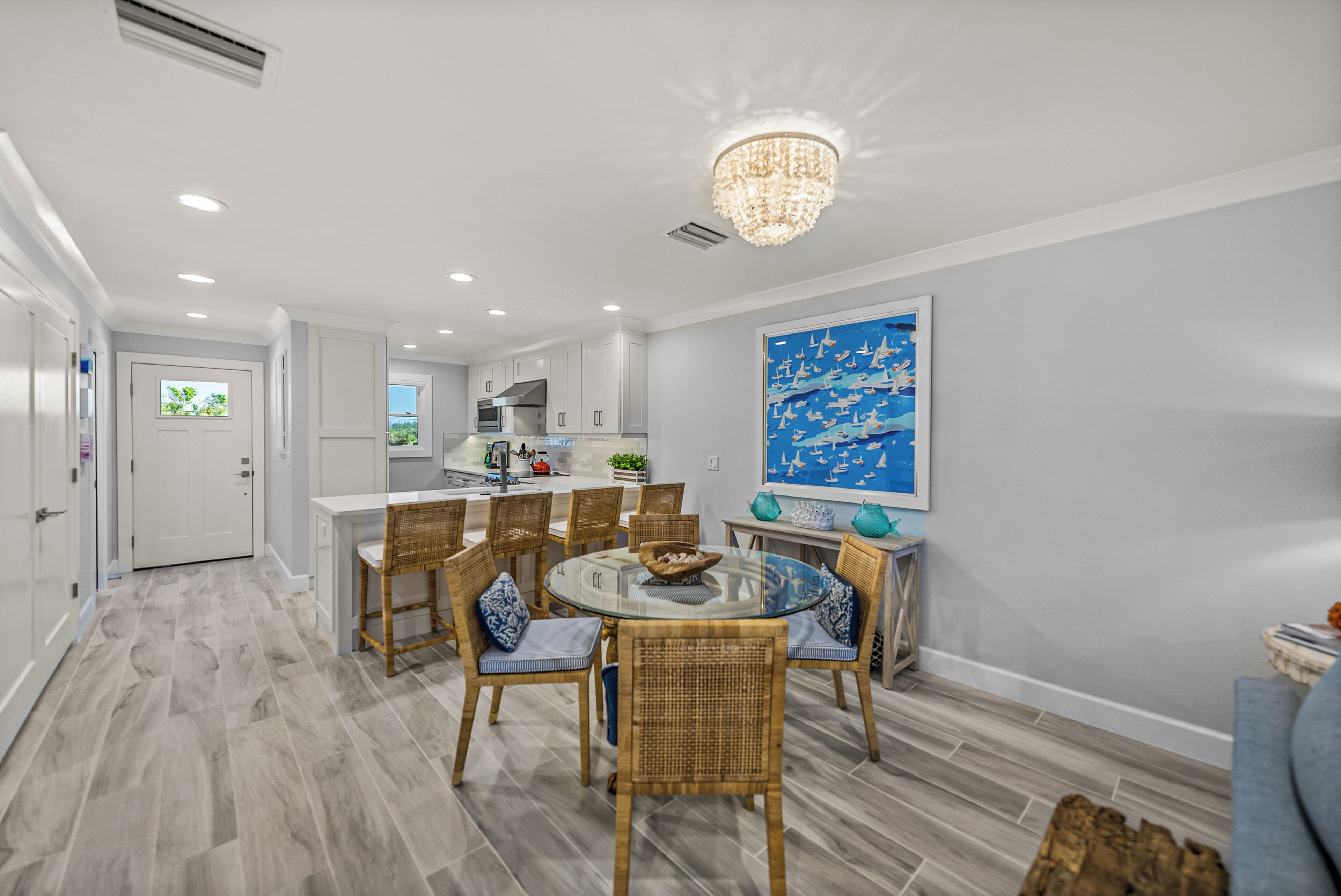 A modern kitchen with white cabinets, a dining area with wicker chairs, and a large blue painting on the wall.
