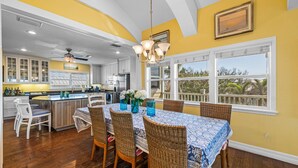 A spacious kitchen with a dining area, featuring a large island, wooden flooring, and a view through the windows.
