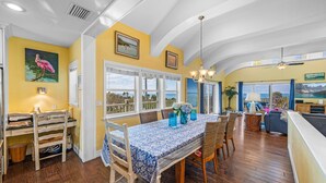 A spacious dining area with a large table, chairs, and a view of the ocean through large windows.