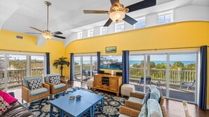 A spacious living area with a large TV, comfortable seating, and a balcony with a view.