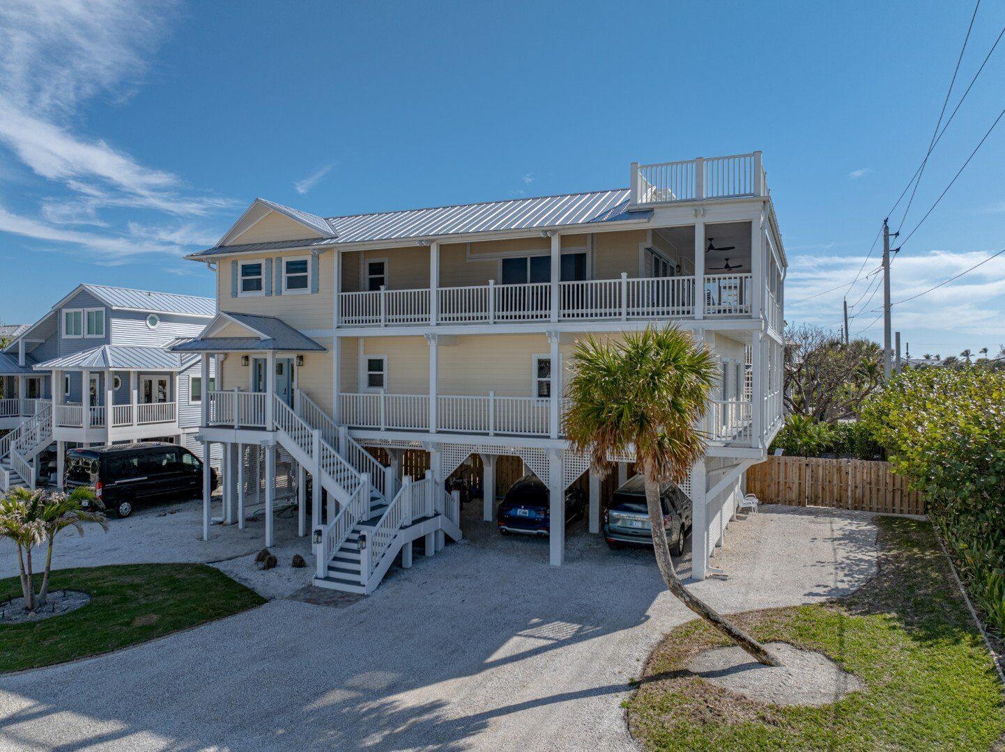 Ein mehrstöckiges Strandhaus mit Balkon, überdachter Veranda und Auffahrt mit geparkten Autos.