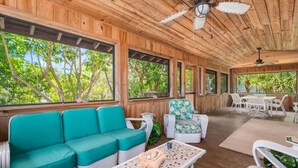 A wooden interior with a teal sofa, a patterned armchair, and a dining area with white furniture.