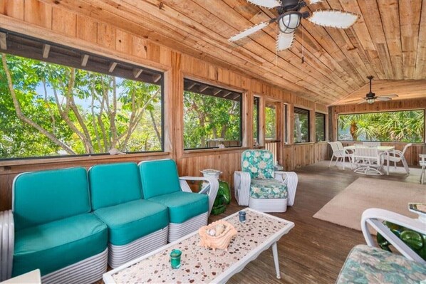 A wooden interior with a teal sofa, a patterned armchair, and a dining area with white furniture.