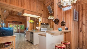 A rustic kitchen with wooden walls, a central island, bar stools, and a large window.