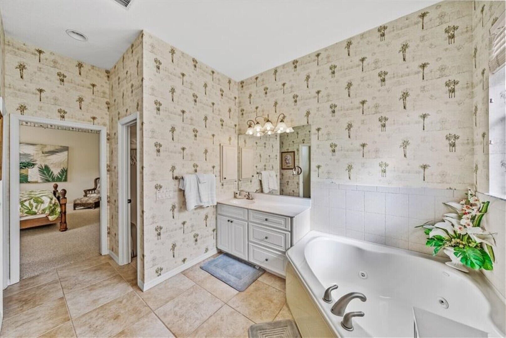 A bathroom with a large bathtub, a vanity with a mirror, and patterned wallpaper.
