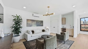 A modern living room with a sofa, two armchairs, a coffee table, a potted plant, and a city view through a large window. - Olive Stone Modern Penthouse Near Mercedes Benz (Atlanta)