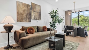 A modern living room with a sofa, a side table, a coffee table, and a dining area with a table and chairs. - Olive Stone Modern Penthouse Near Mercedes Benz (Atlanta)