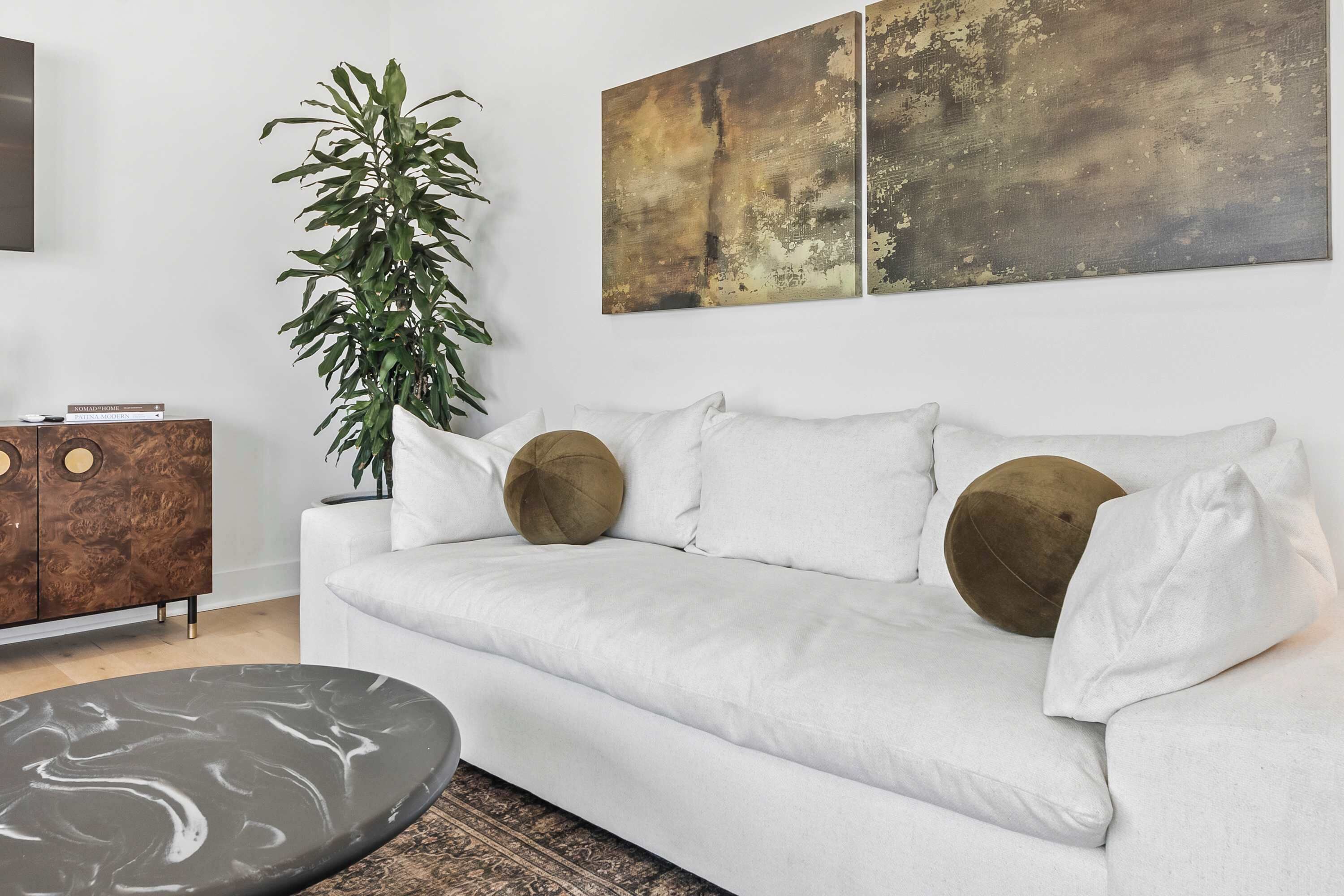 A modern living room with a white sofa, a round coffee table, a large green plant, and abstract artwork on the wall.