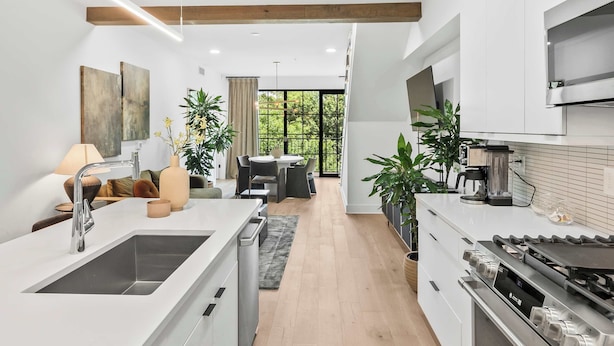 A modern kitchen with a large island, built-in appliances, and a dining area with a view. - Olive Stone Modern Penthouse Near Mercedes Benz (Atlanta)