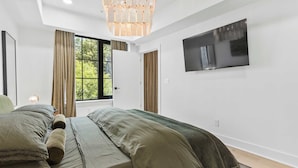 A bedroom with a bed, a TV mounted on the wall, and a window with curtains. - Olive Stone Modern Penthouse Near Mercedes Benz (Atlanta)