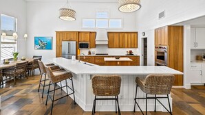 A spacious kitchen with a large island, wooden cabinets, stainless steel appliances, and a dining area with wicker chairs.