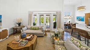 A spacious living room with a large sofa, a coffee table, and a dining area with wicker chairs.